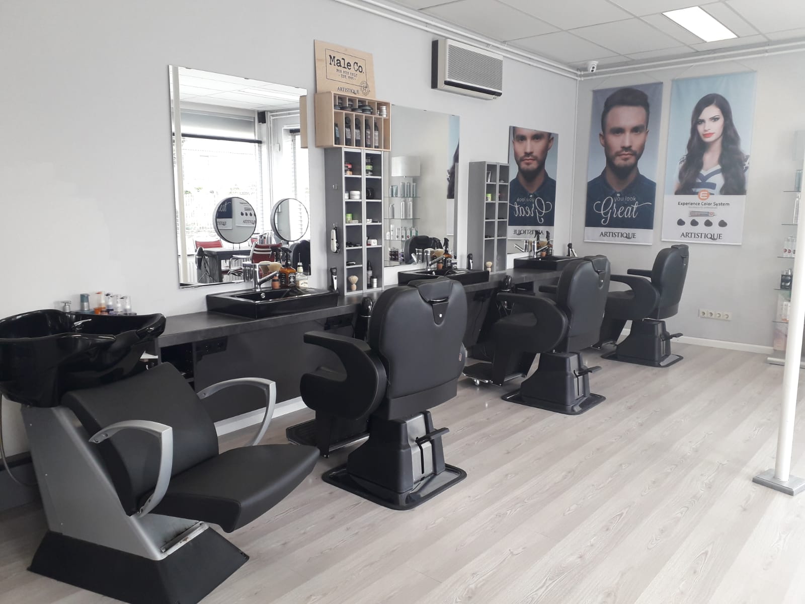 De lichte kapsalon met zwarte kappersstoelen en grote spiegels